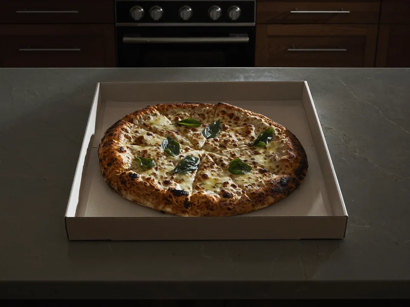 Holzofen-Pizza mit Käse und Basilikum im unbedruckten Karton auf der Küchenarbeitsplatte