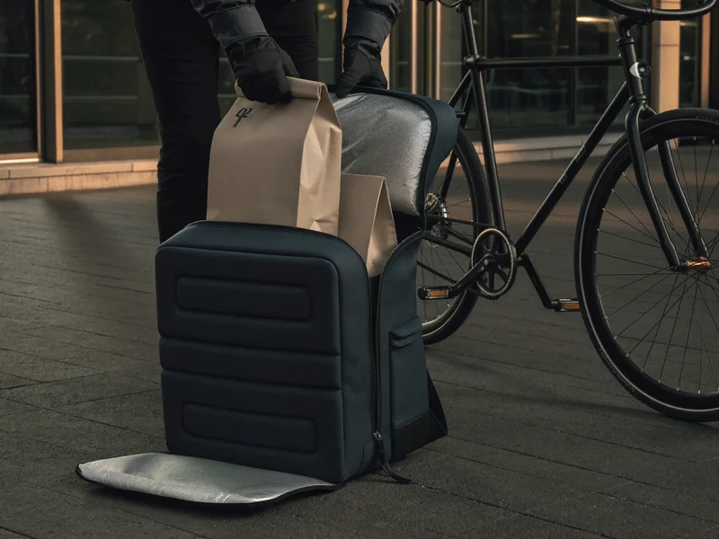 Kurierhände verstauen verschlossene Papiertüten in einem isolierten Lieferrucksack neben einem Fahrrad