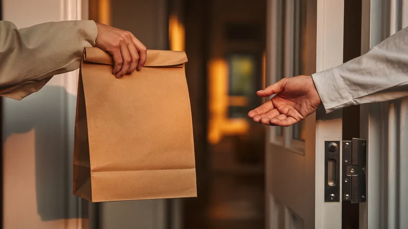 Übergabe einer schlichten Papiertüte an der Wohnungstür im warmen Flurlicht